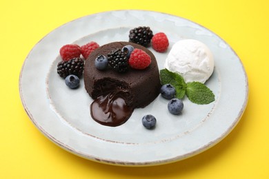 Photo of Delicious chocolate fondant served with fresh berries and ice cream on yellow background, closeup