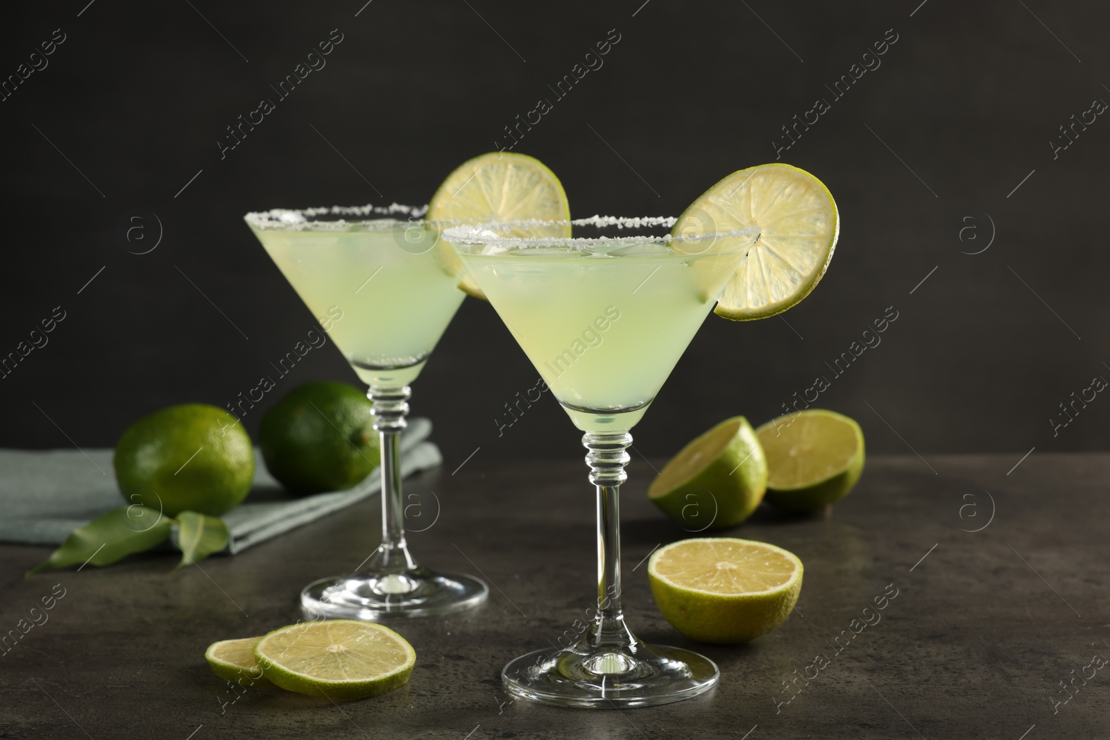 Photo of Delicious Margarita cocktail in glasses and limes on grey table