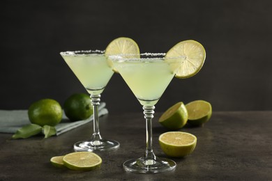 Delicious Margarita cocktail in glasses and limes on grey table