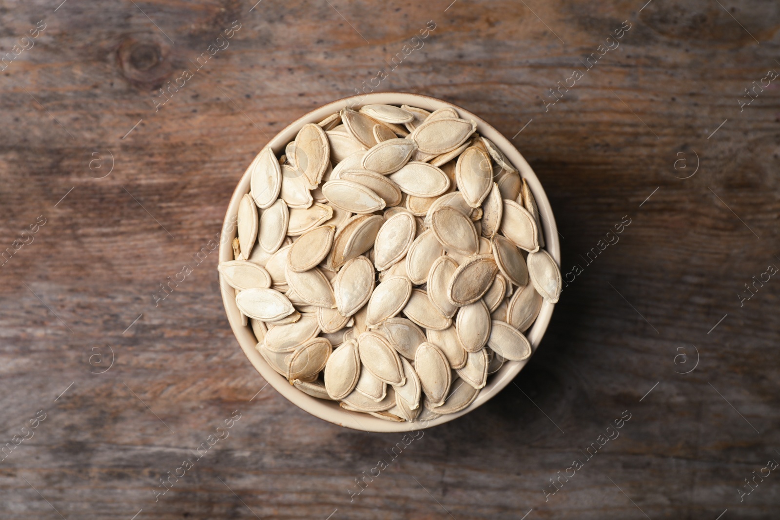 Photo of Raw pumpkin seeds in bowl on wooden background, top view