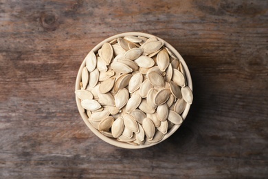 Raw pumpkin seeds in bowl on wooden background, top view