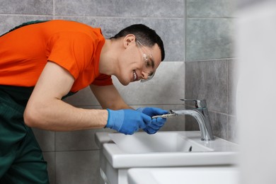 Smiling plumber repairing faucet with spanner in bathroom