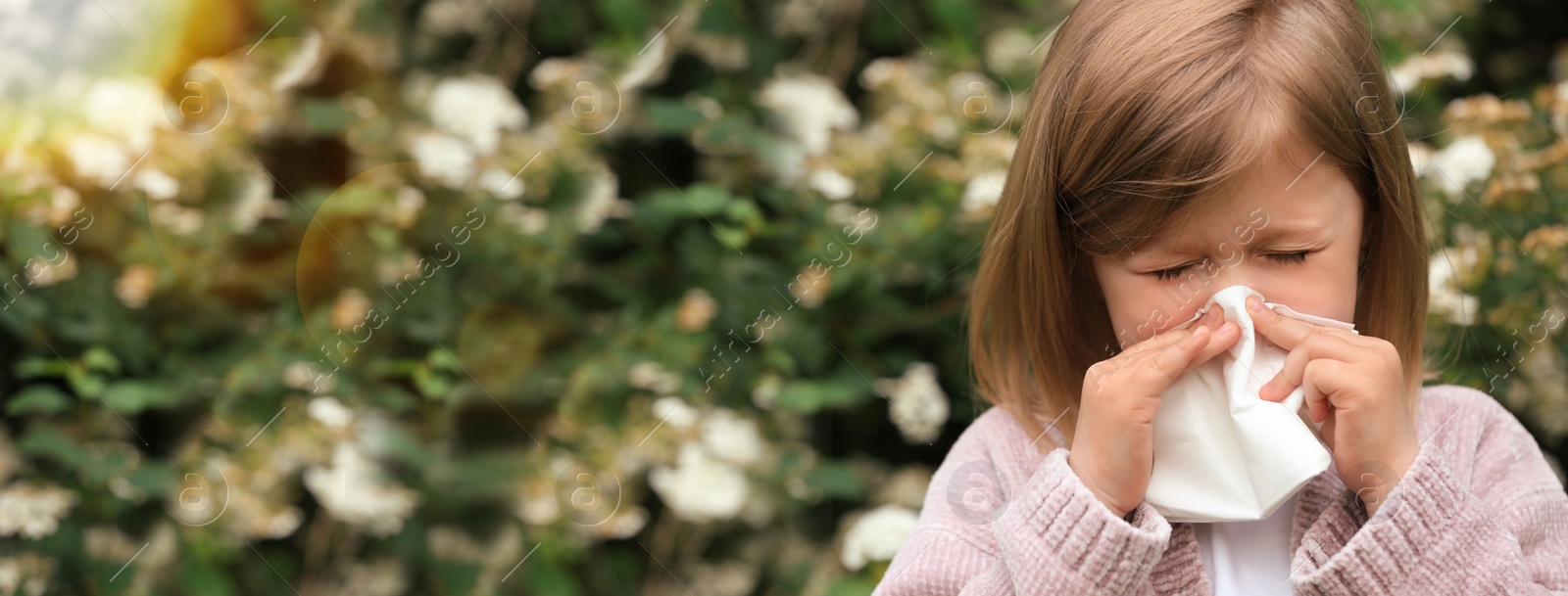 Image of Little girl suffering from seasonal pollen allergy near blossoming tree on spring day. Banner design with space for text