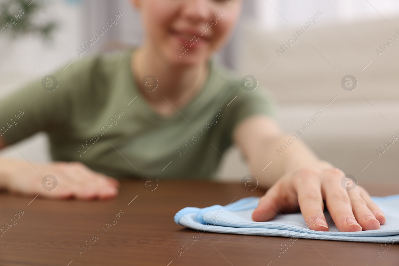 Photo of Woman with microfiber cloth cleaning wooden table in room, closeup