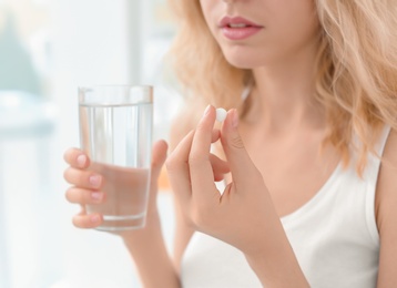 Young woman with pill and glass of water indoors