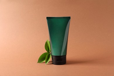 Tube of men's facial cream and green leaves on orange background