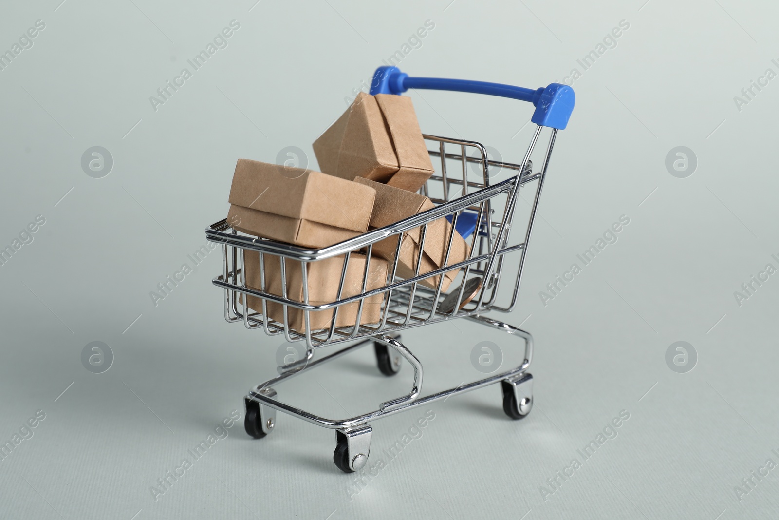 Photo of Small metal shopping cart with cardboard boxes on light background