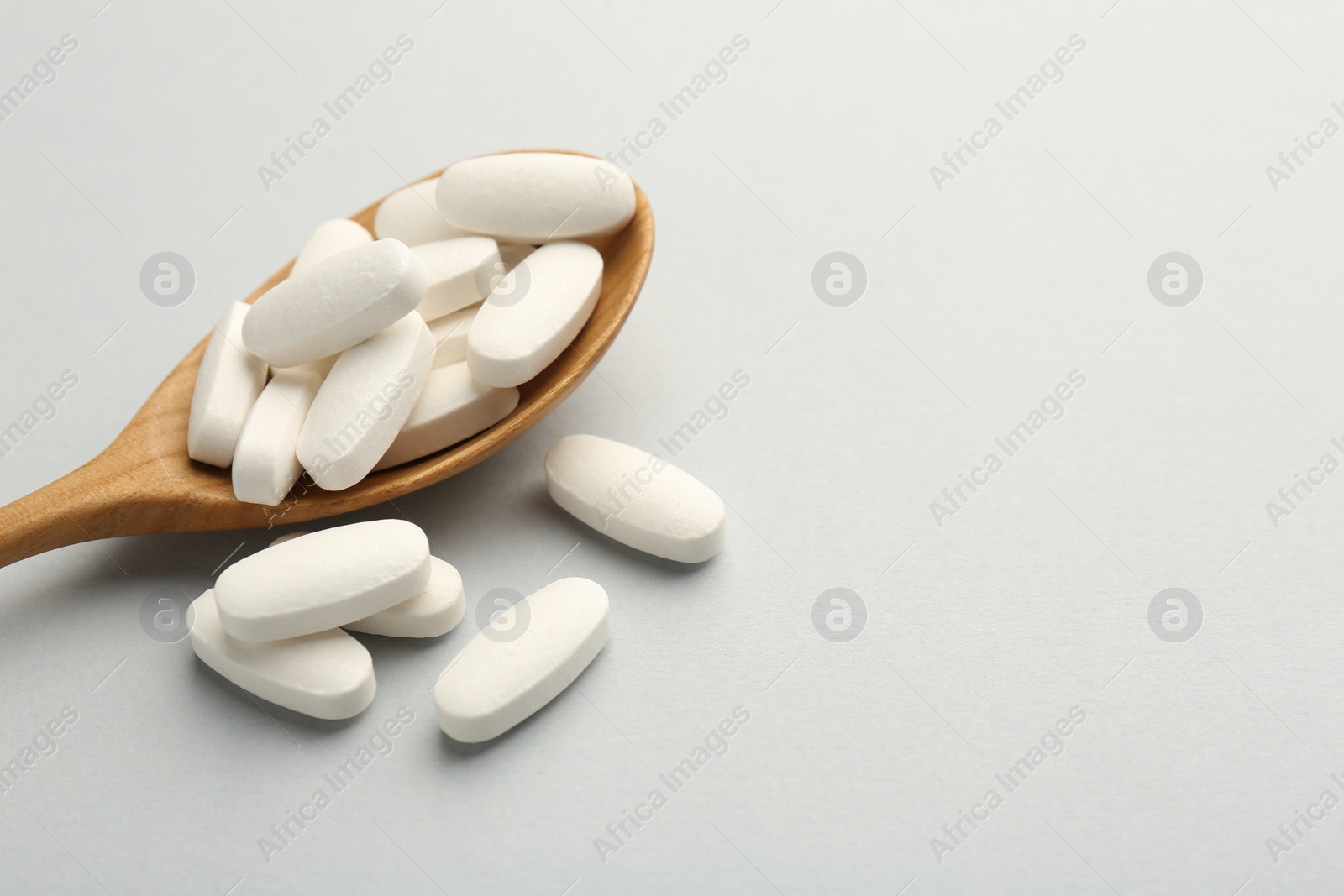 Photo of Vitamin pills and wooden spoon on light grey background, closeup with space for text. Health supplement