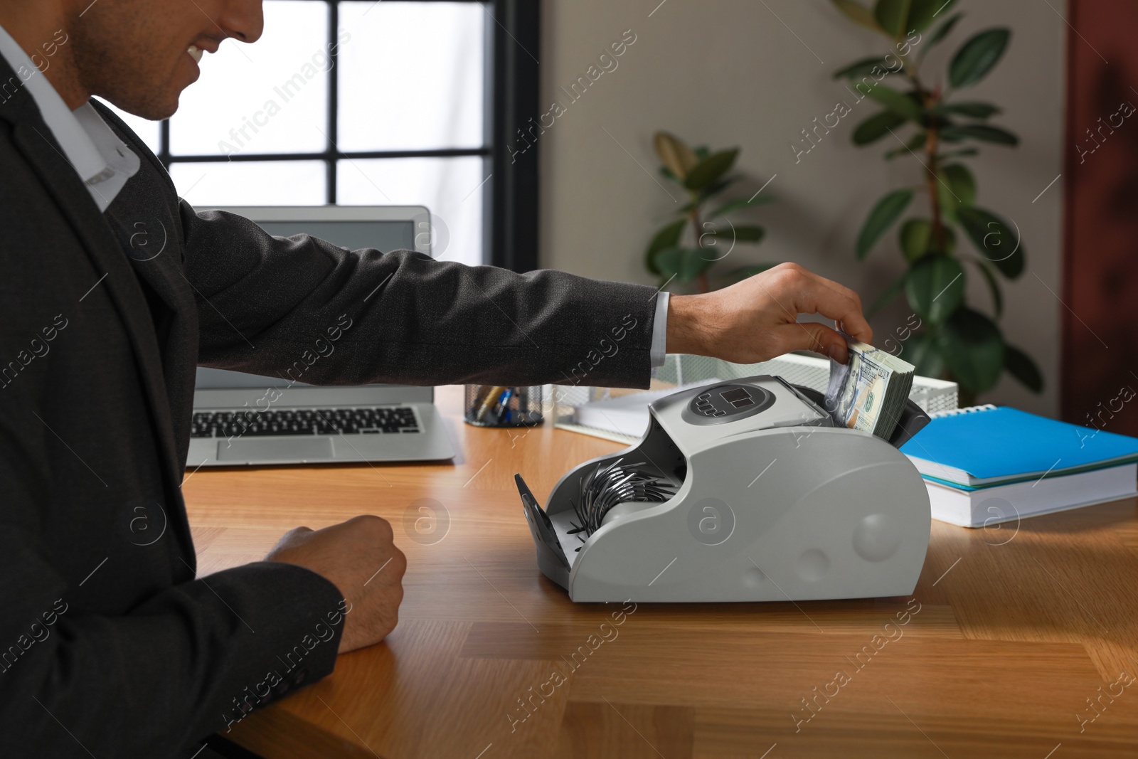 Photo of Man putting money into banknote counter at wooden table indoors, closeup