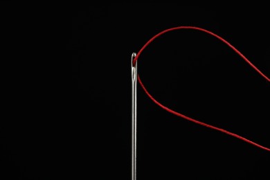 Photo of Sewing needle with red thread on black background, closeup