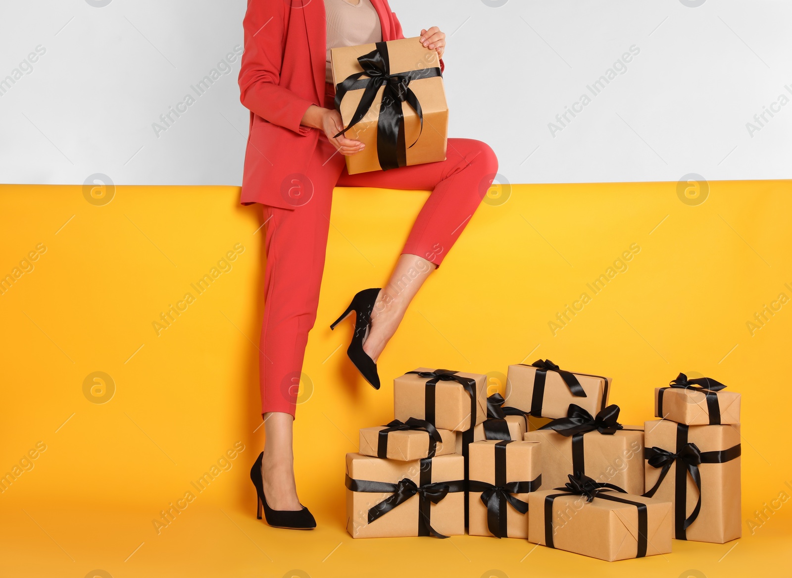 Photo of Woman with gift boxes sitting on yellow background, closeup. Black Friday