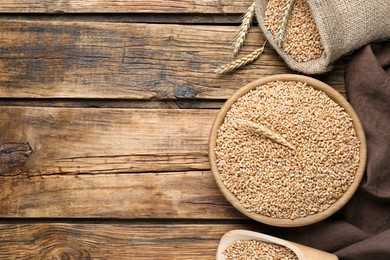 Photo of Ears of wheat and grains on wooden table, flat lay. Space for text