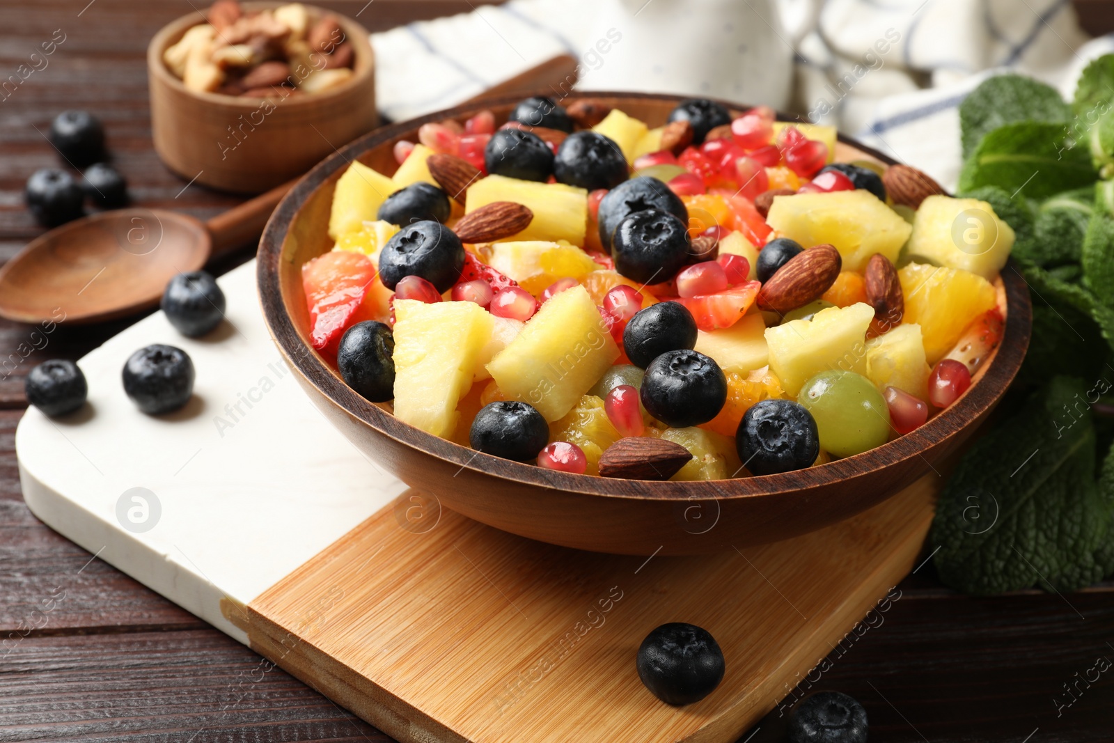 Photo of Delicious fruit salad in bowl, berries, nuts and fresh mint on wooden table
