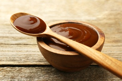 Tasty barbeque sauce in bowl and spoon on wooden table, closeup