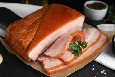 Photo of Delicious smoked bacon with parsley and salt on black table, closeup