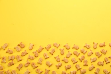 Photo of Delicious goldfish crackers on yellow background, flat lay. Space for text