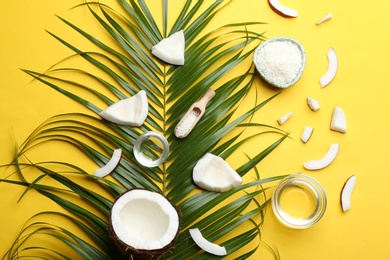Photo of Bowls of natural organic oil and coconuts on yellow background, flat lay