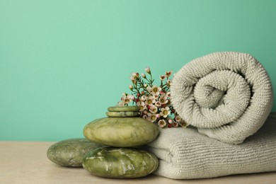 Photo of Composition with spa stones, towels and flowers on beige table against turquoise background. Space for text