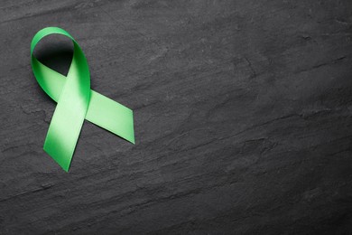 Photo of World Mental Health Day. Green ribbon on black background, top view with space for text