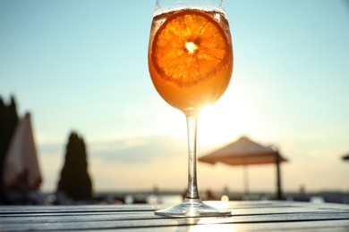 Glass of fresh summer cocktail on wooden table outdoors at sunset, low angle view