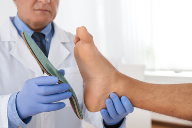 Photo of Male orthopedist fitting insole on patient's foot in clinic, closeup