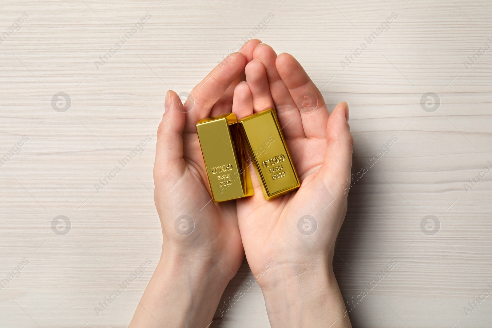 Photo of Woman holding gold bars on white wooden table, top view