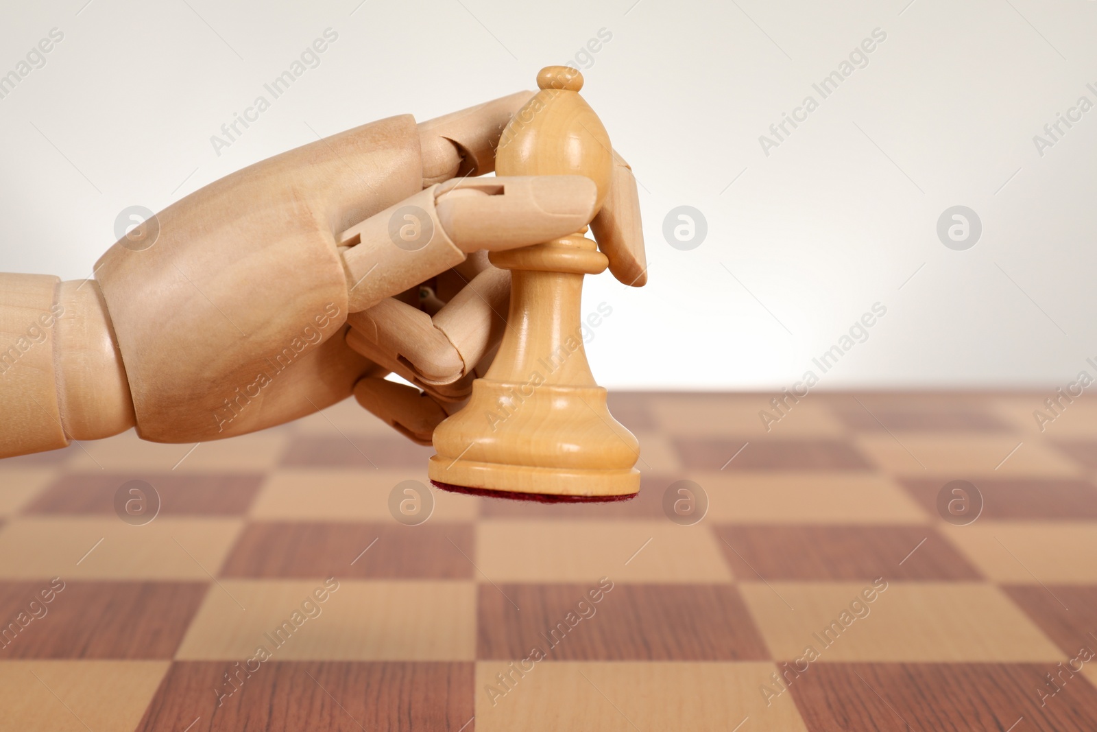 Photo of Robot with chess piece above board against light background, space for text. Wooden hand representing artificial intelligence