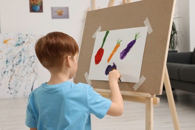 Photo of Little boy painting in studio, back view. Using easel to hold canvas