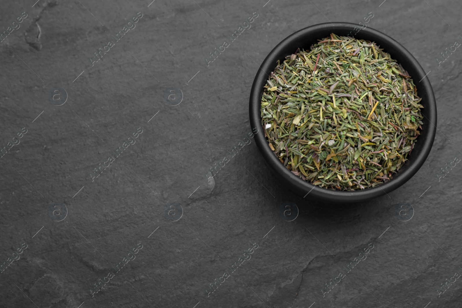 Photo of Bowl with dried thyme on black table, top view. Space for text