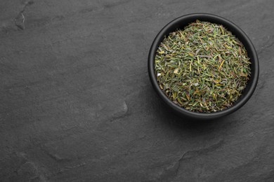 Bowl with dried thyme on black table, top view. Space for text