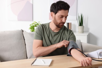 Photo of Man measuring blood pressure at wooden table in room