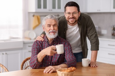 Happy son and his dad at wooden table in kitchen