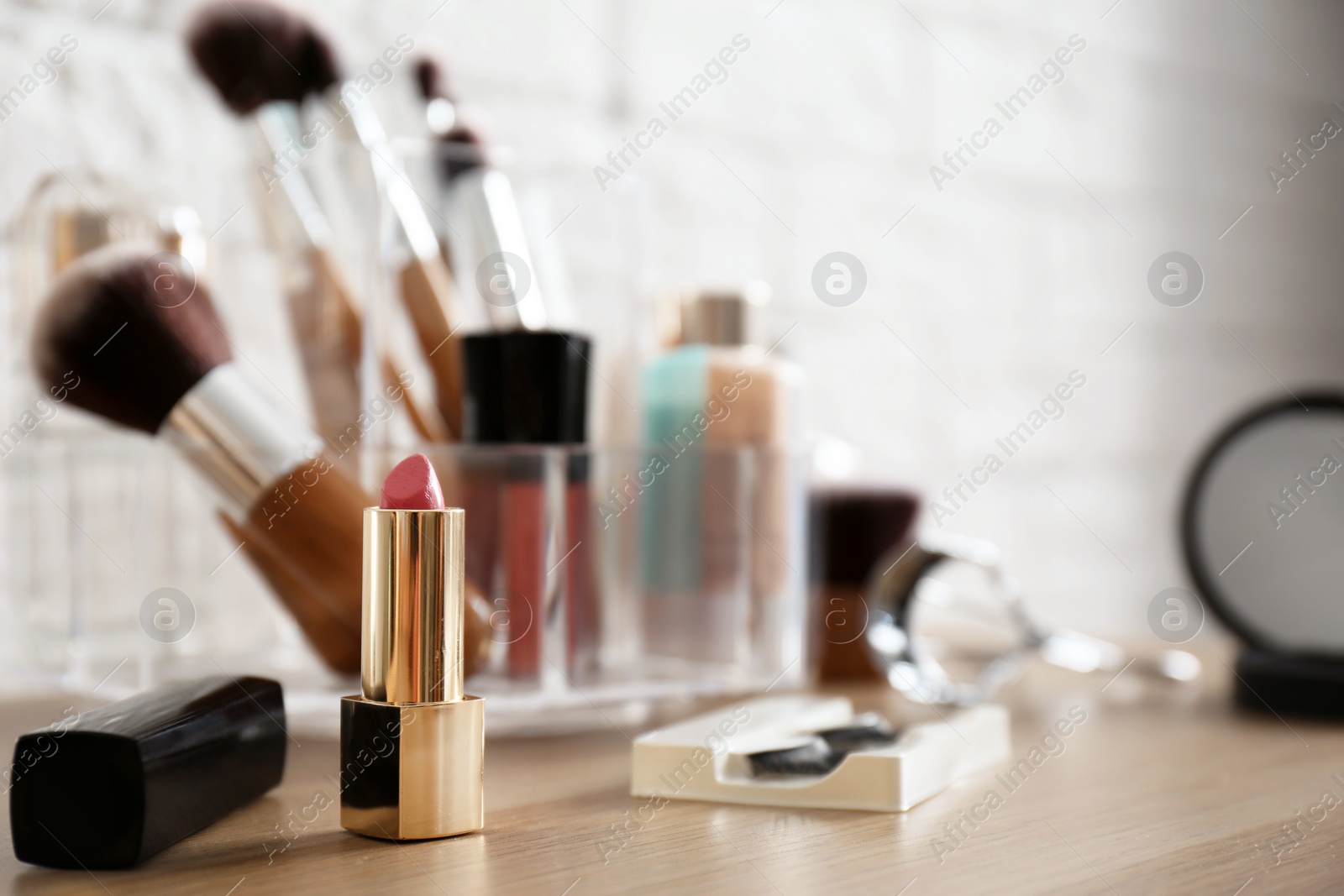 Photo of Lipstick and organizer with cosmetic products for makeup on table near brick wall