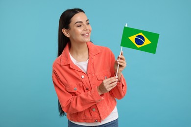 Happy young woman with flag of Brazil on light blue background