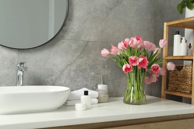 Photo of Vase with beautiful pink tulips and toiletries near sink in bathroom