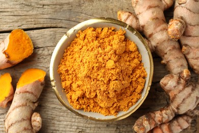 Photo of Aromatic turmeric powder and raw roots on wooden table, flat lay