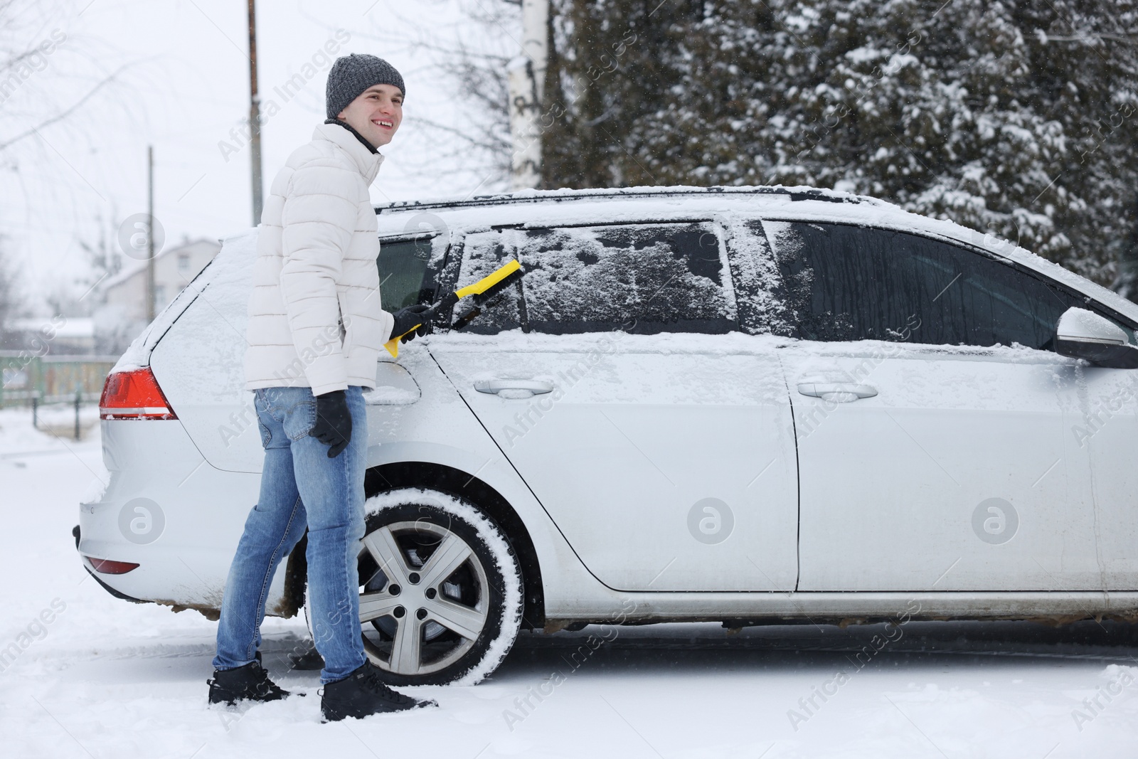 Photo of Man cleaning snow from car with brush outdoors