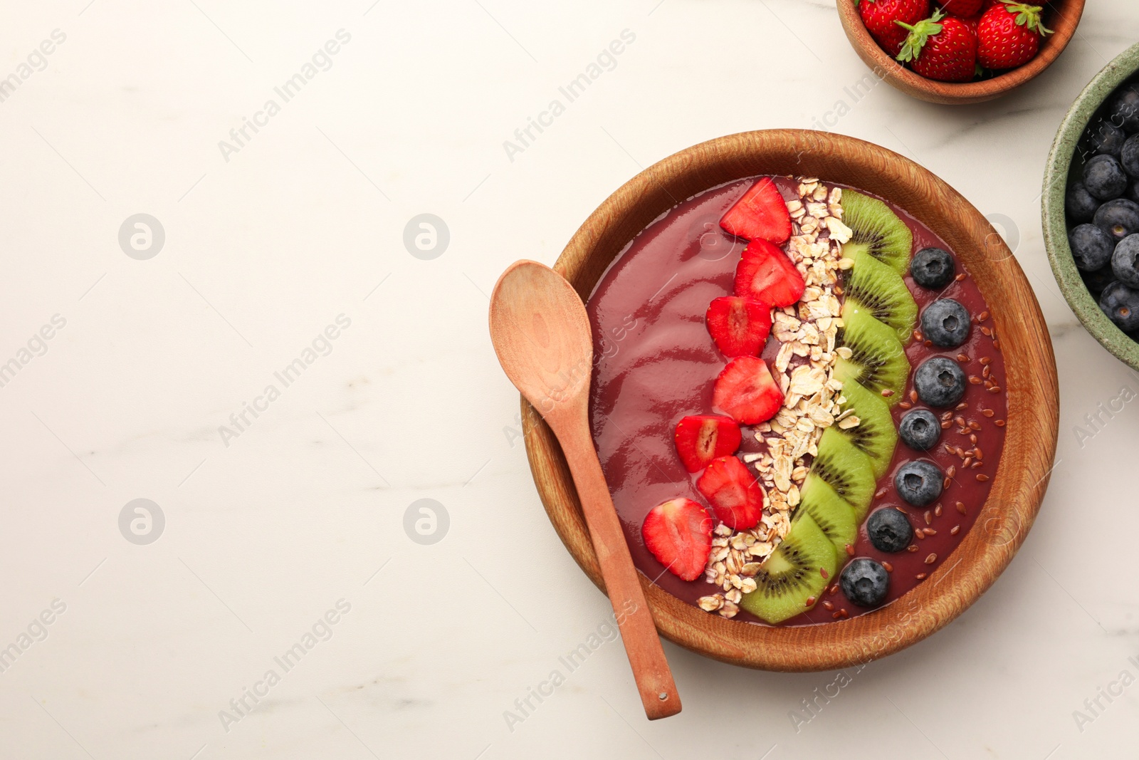 Photo of Bowl of delicious smoothie with fresh blueberries, strawberries, kiwi slices and oatmeal on white marble table, flat lay. Space for text