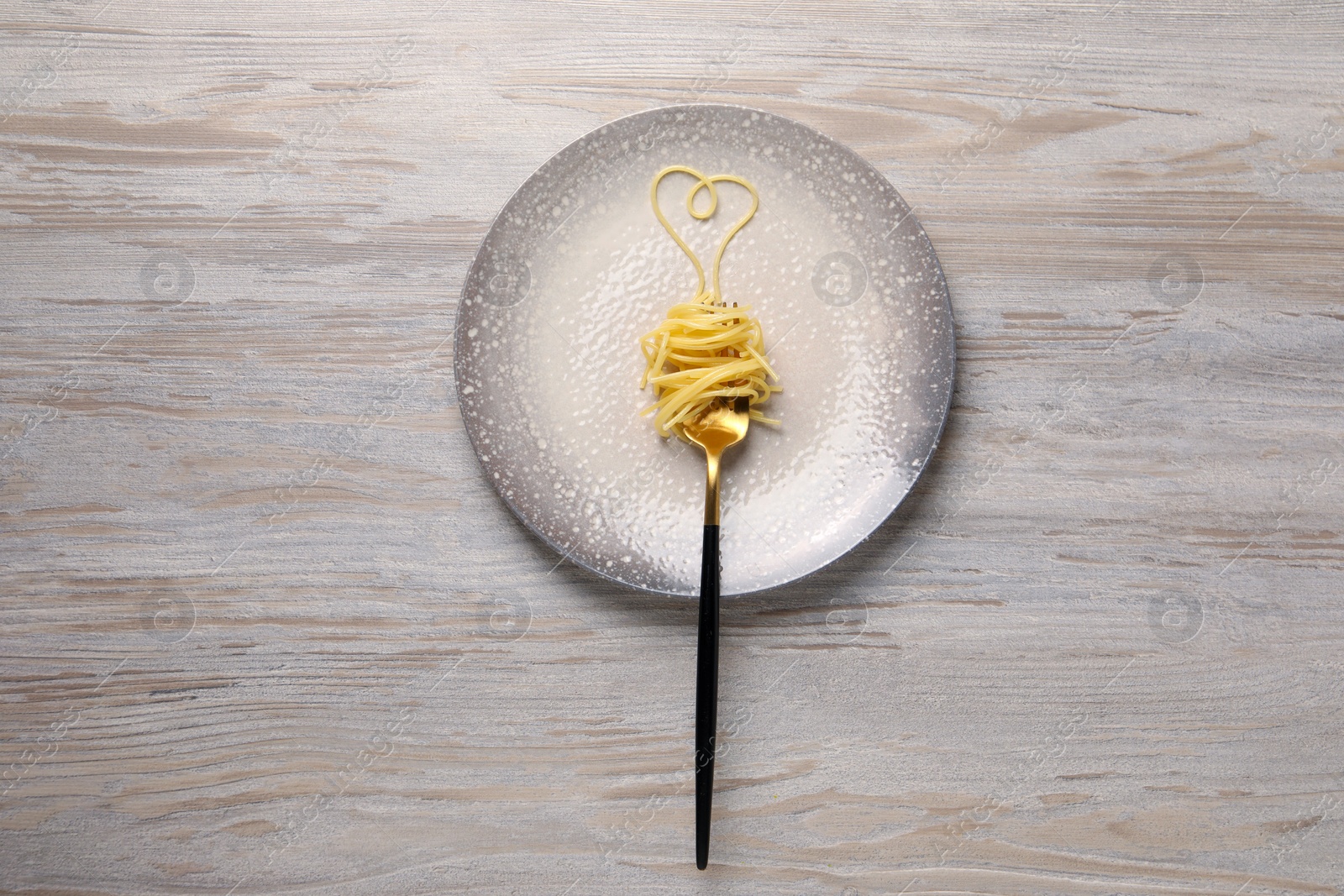 Photo of Heart made with spaghetti and fork on light wooden table, top view