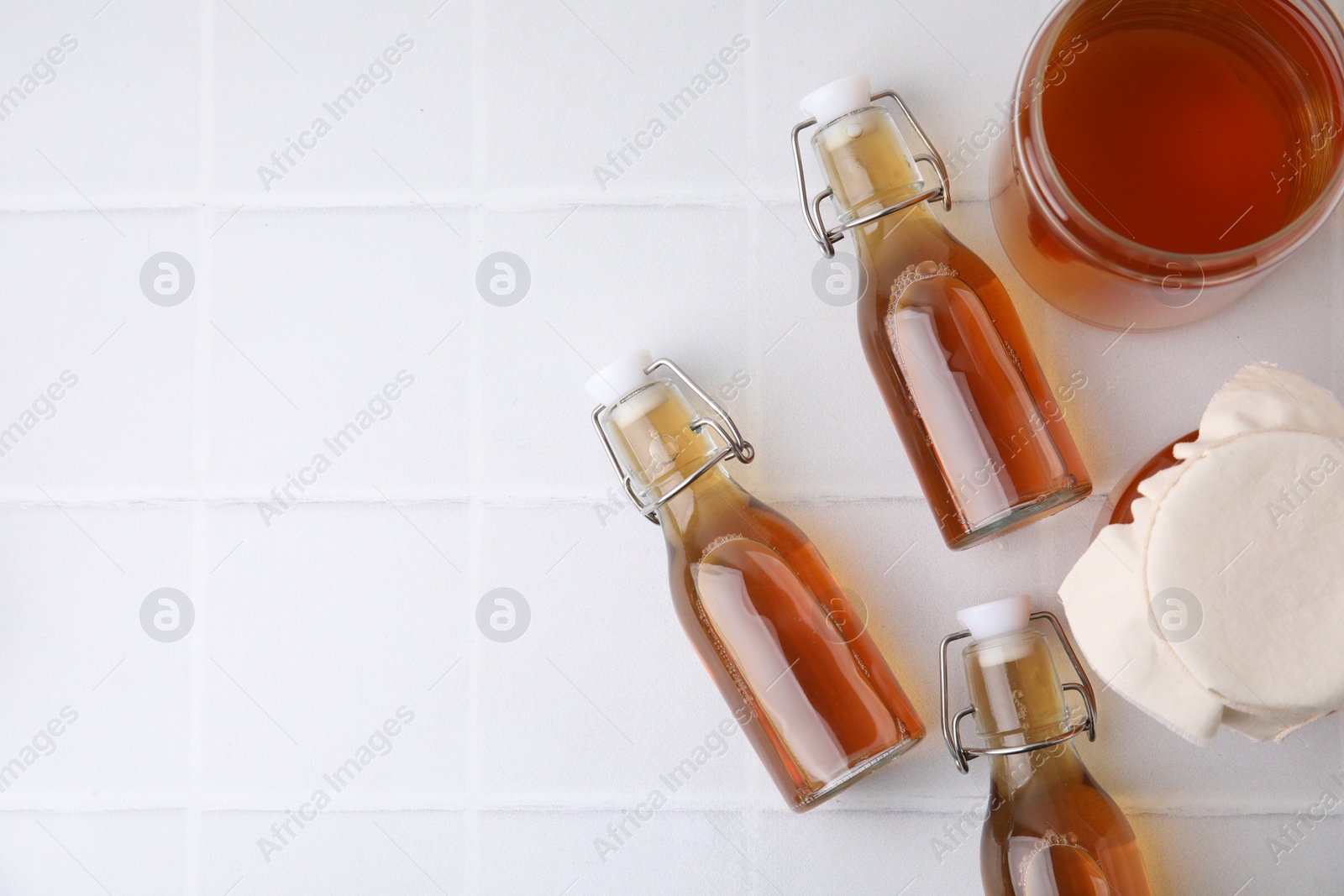 Photo of Tasty kombucha on white tiled table, flat lay. Space for text