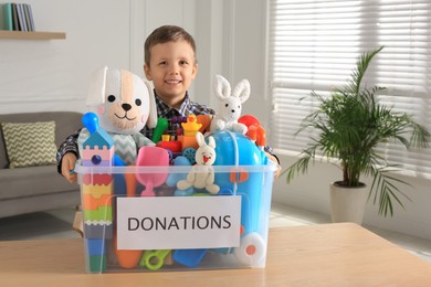 Photo of Cute little boy holding donation box with toys at home, space for text