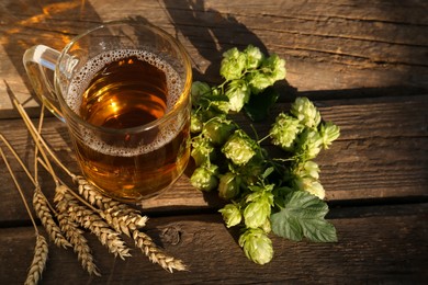 Photo of Mug with beer, fresh hops and ears of wheat on wooden table, above view