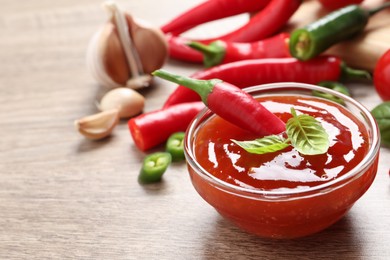 Photo of Spicy chili sauce with basil on wooden table, space for text