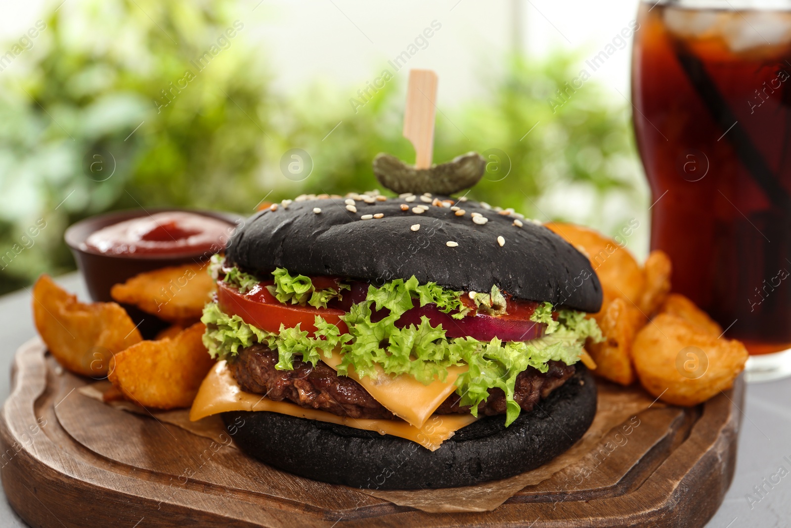 Photo of Juicy black burger and french fries on wooden board, closeup