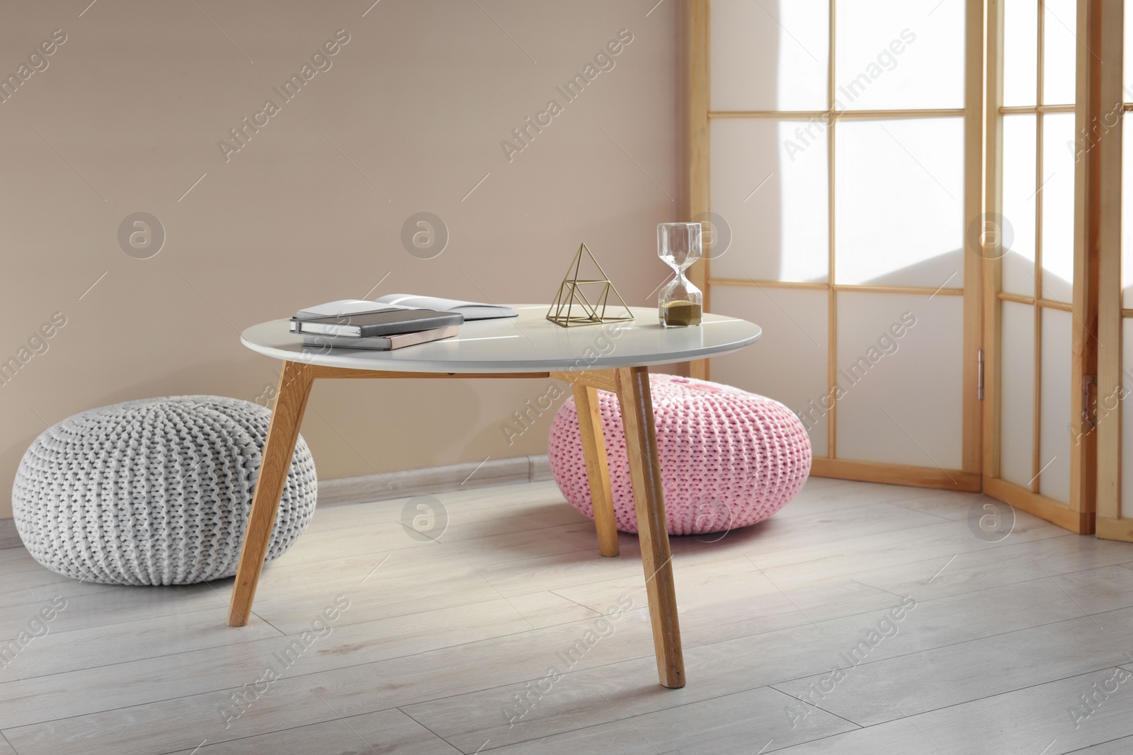 Photo of White table with books, golden pyramid and hourglass in room. Interior design
