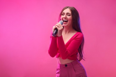 Emotional woman with microphone singing on pink background. Space for text