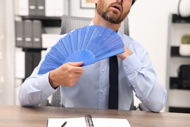 Businessman with blue hand fan at table in office, closeup