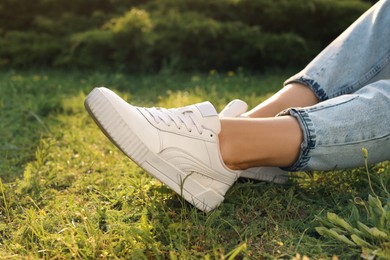 Photo of Woman in jeans and white shoes relaxing on green grass, closeup