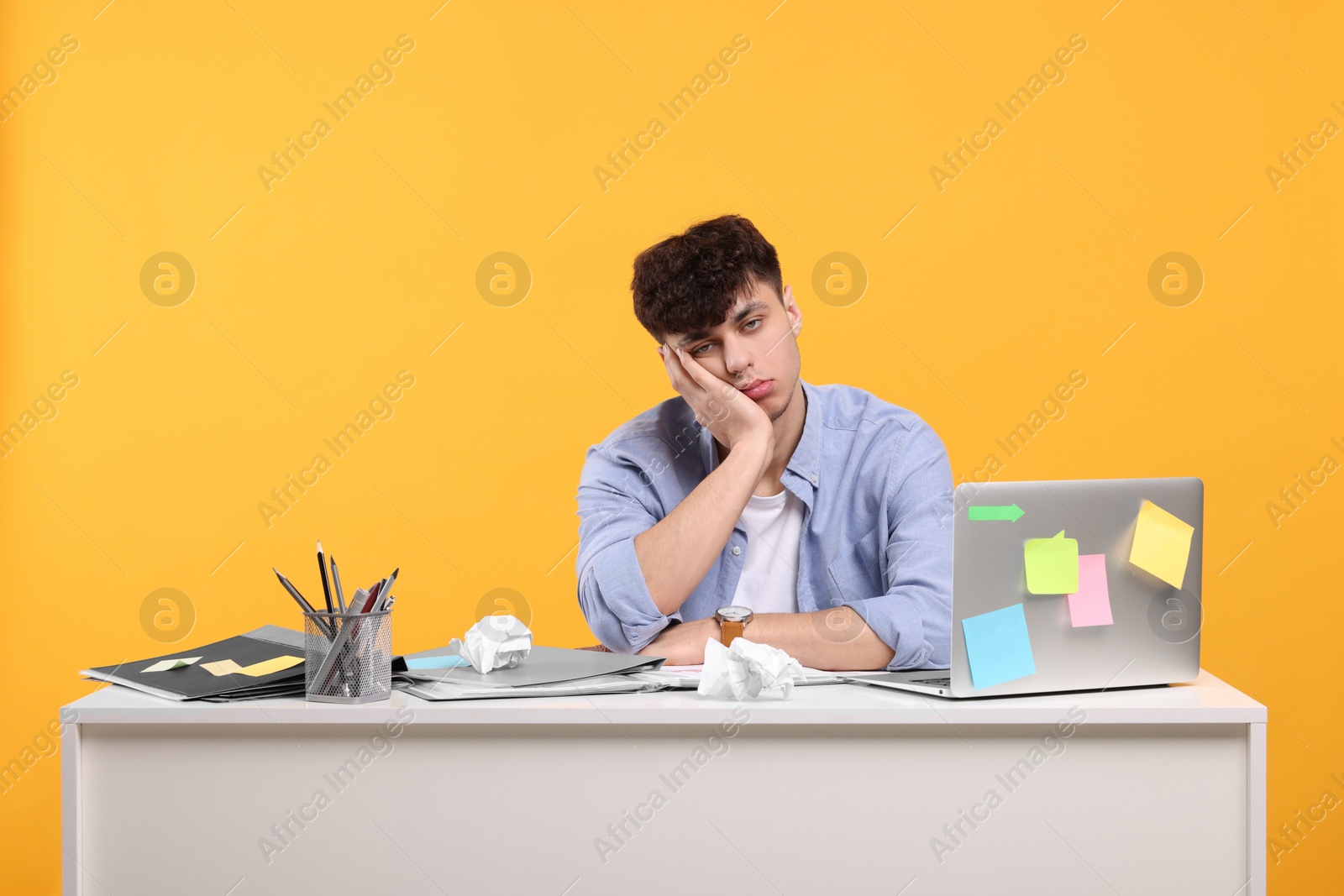 Photo of Tired young man working at white table on orange background. Deadline concept