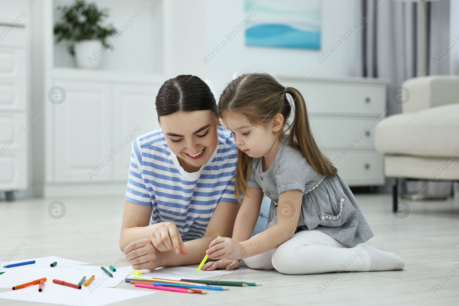 Photo of Mother and her little daughter drawing with colorful markers on floor at home